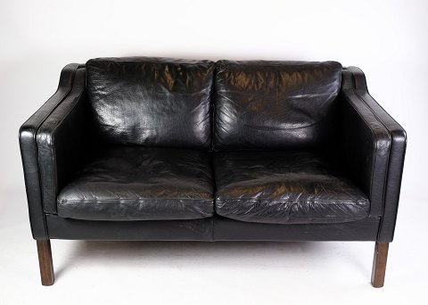 En to personers sofa betrukket med sort læder fremstillet af Stouby Møbelfabrik 
i 1960