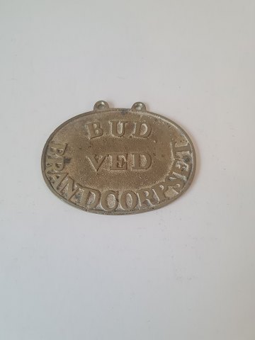 Badge in brass with the text "Bud ved brandcorpset"